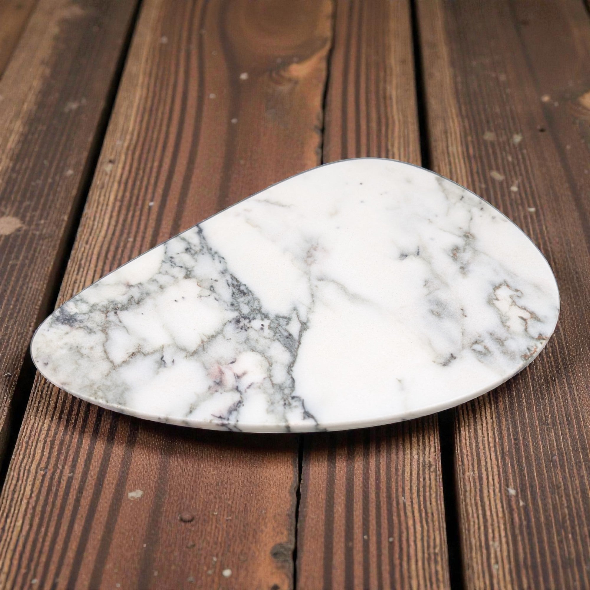 White marble vanity tray with gray veining in an organic teardrop shape on dark wood background.