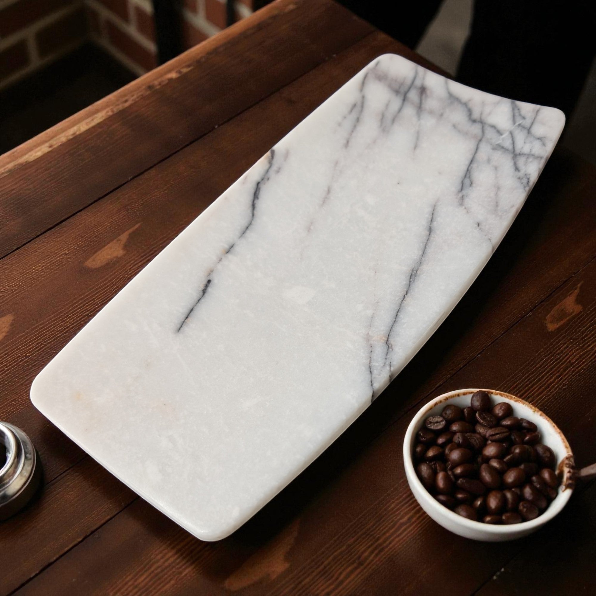 Handcrafted rectangular white marble serving tray with natural grey veining placed on a rustic wooden table beside a bowl of coffee beans.