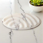 Oval marble soap dish with sculptural form, white stone with natural veining, polished
surface, luxury bathroom accessory, artisan-crafted

