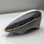 Ceramic shoe with black and gold design on a white surface