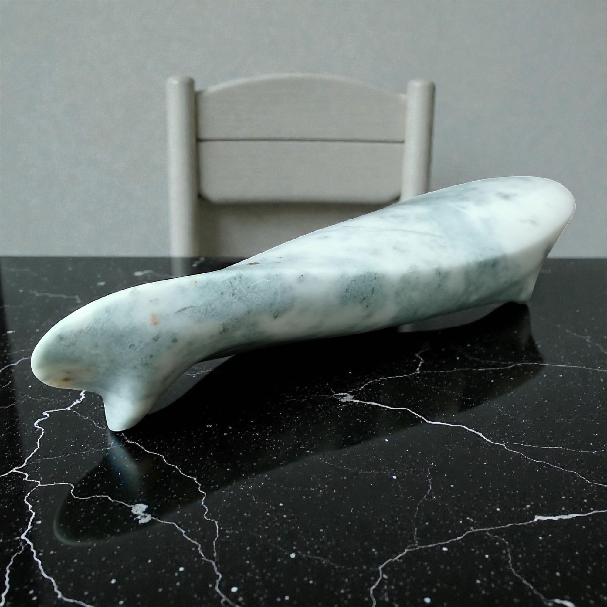 Marble-textured object on a black marble surface with a white chair in the background.