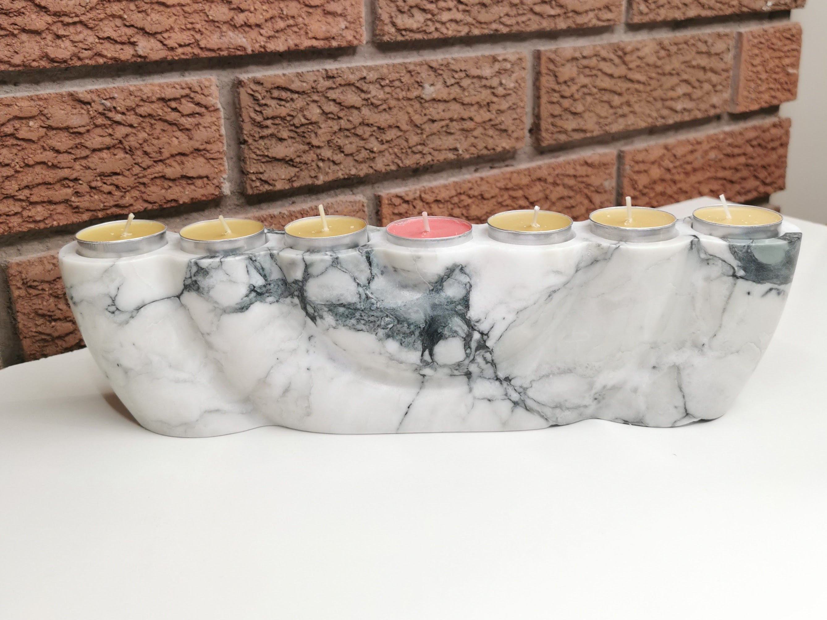 Marble-patterned candle holder with colorful candles against a brick wall.