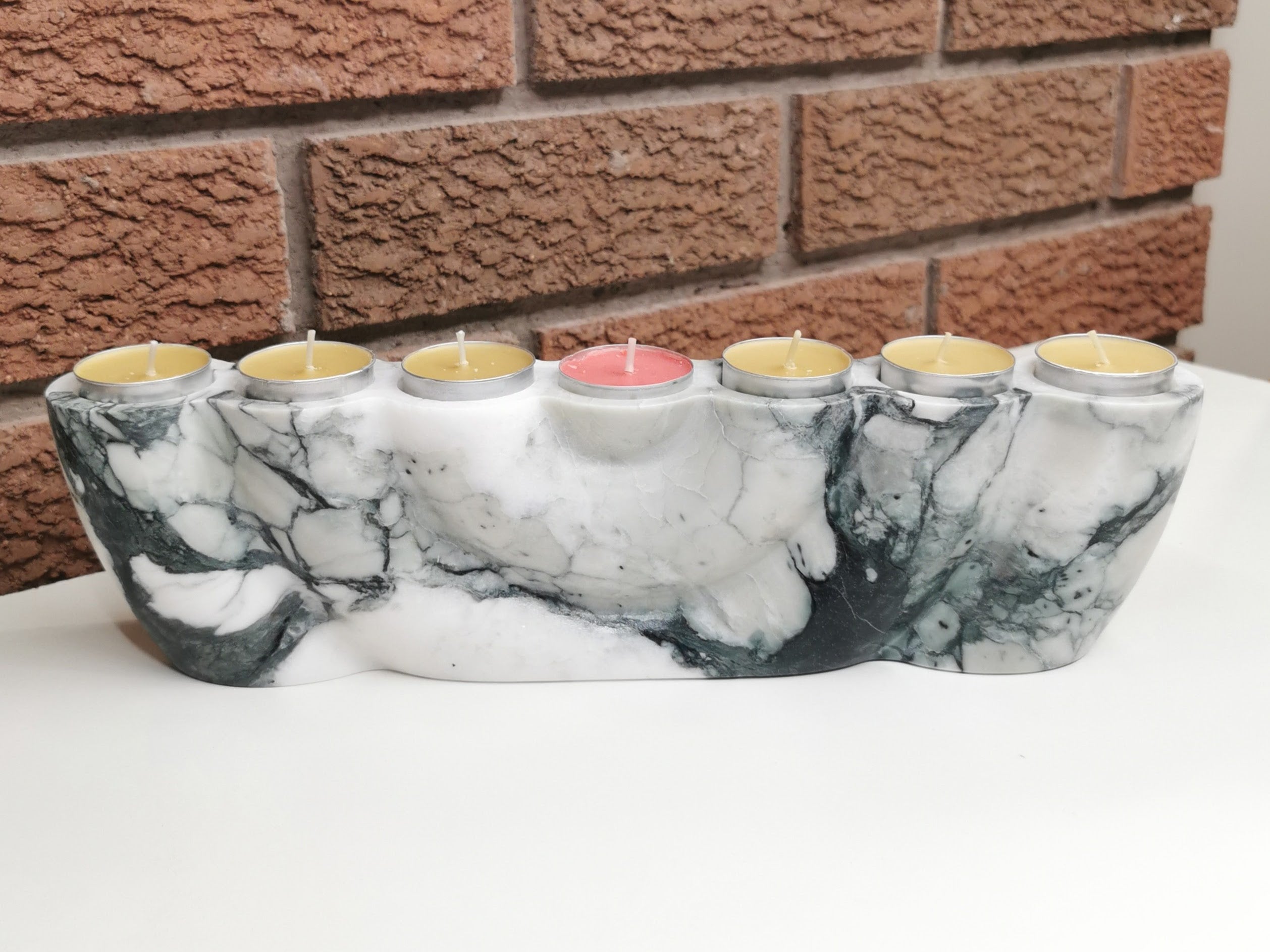 Marble-patterned candle holder with lit candles against a brick wall background