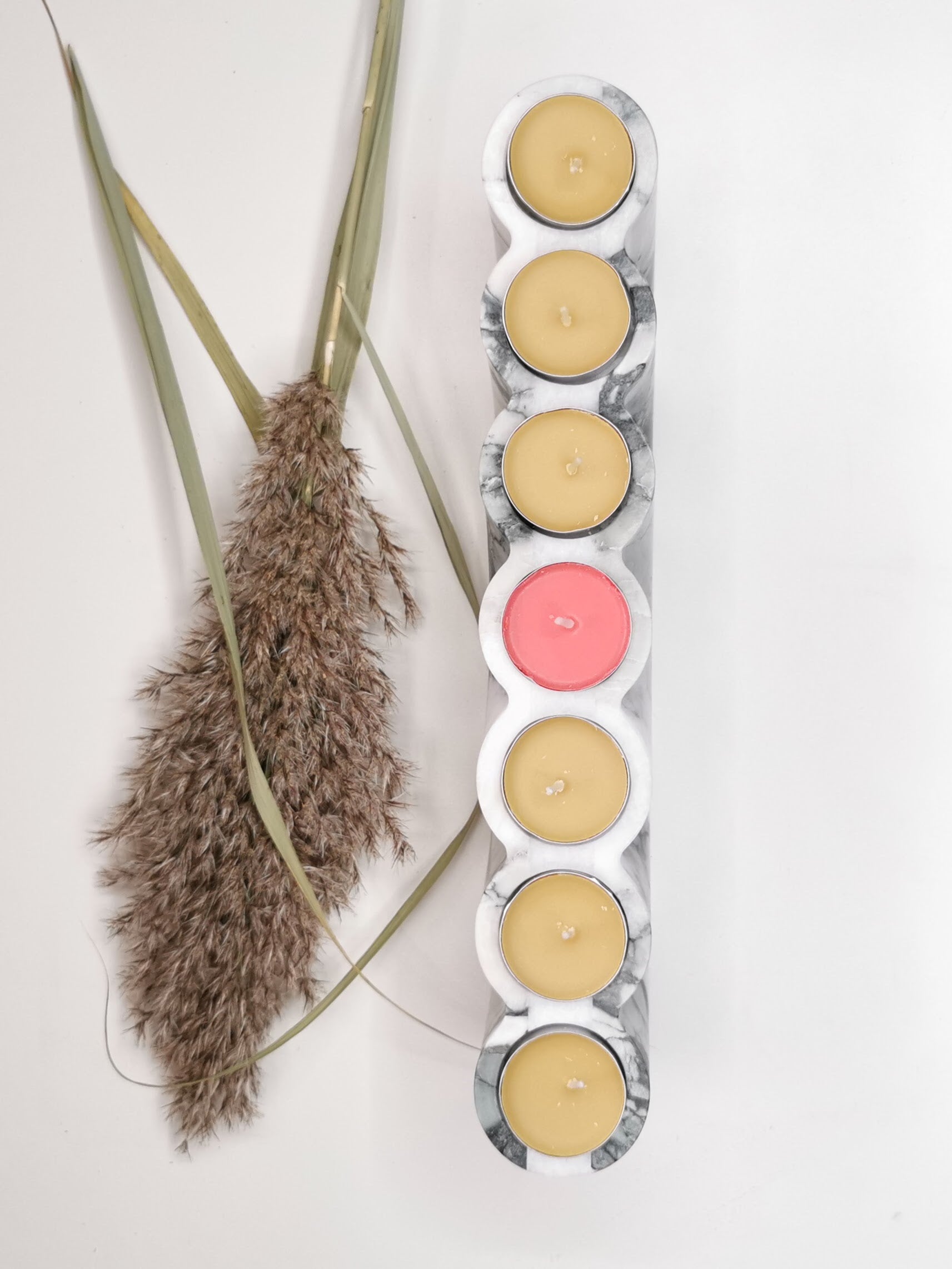 Set of colorful candles in a holder with dried plants on a light background