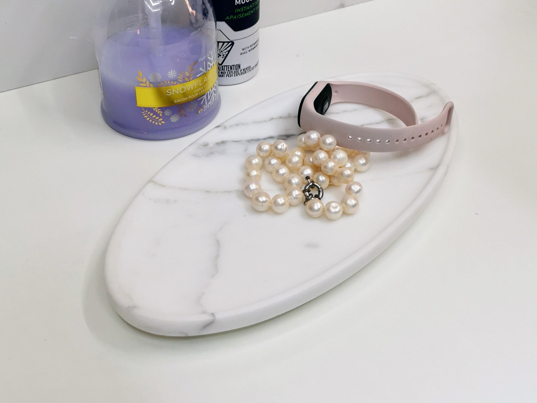 Pearl necklace and pink smartwatch on a marble tray with bottles in the background
