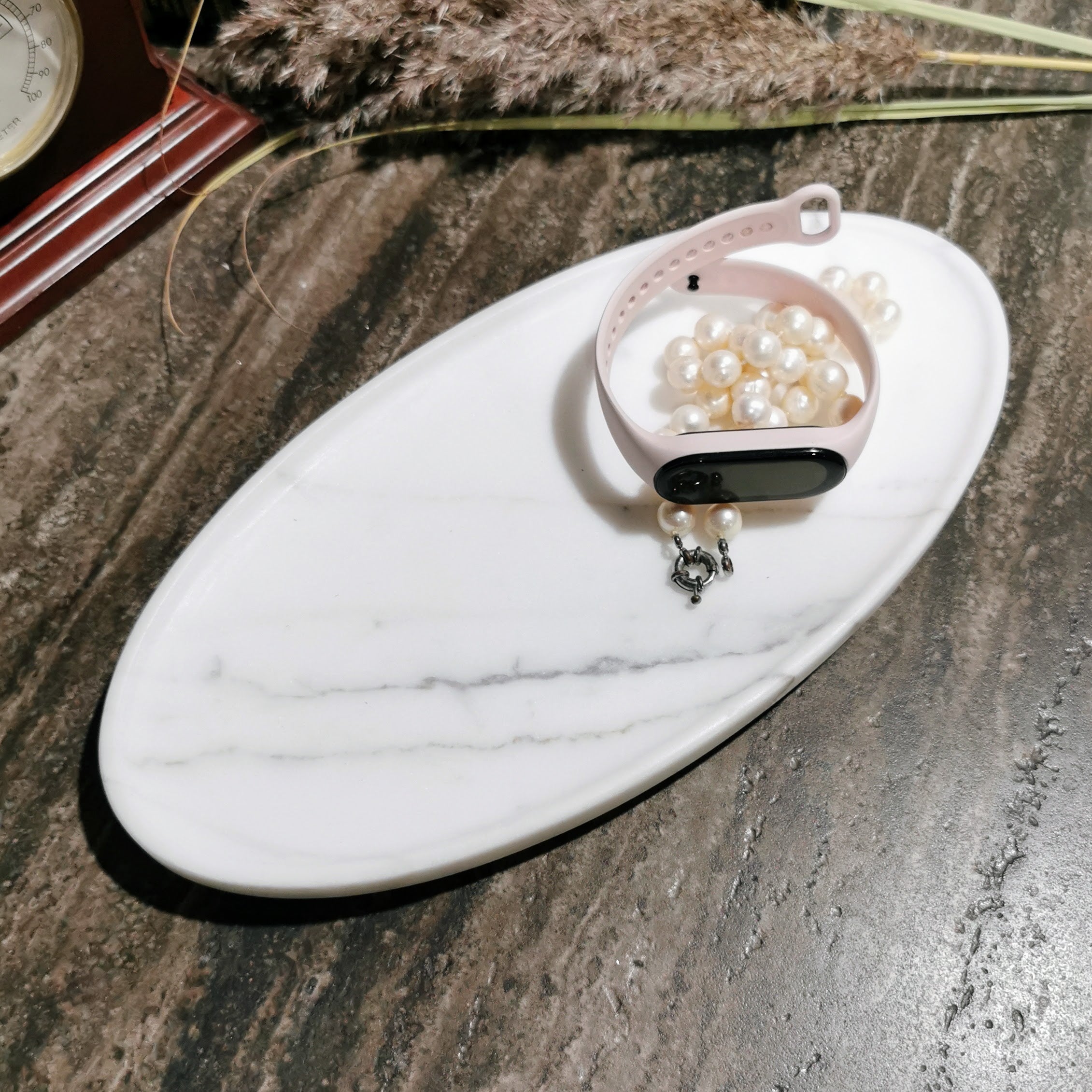 Pink smartwatch with pearls on a marble tray on a stone surface