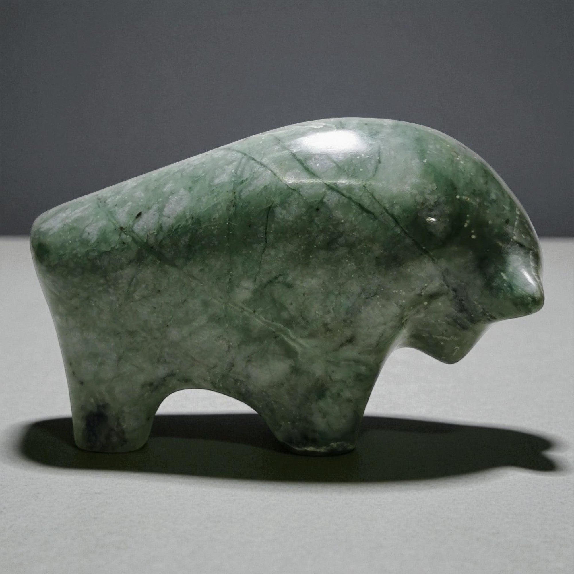 Green stone sculpture of a bear on a gray surface with a dark background
