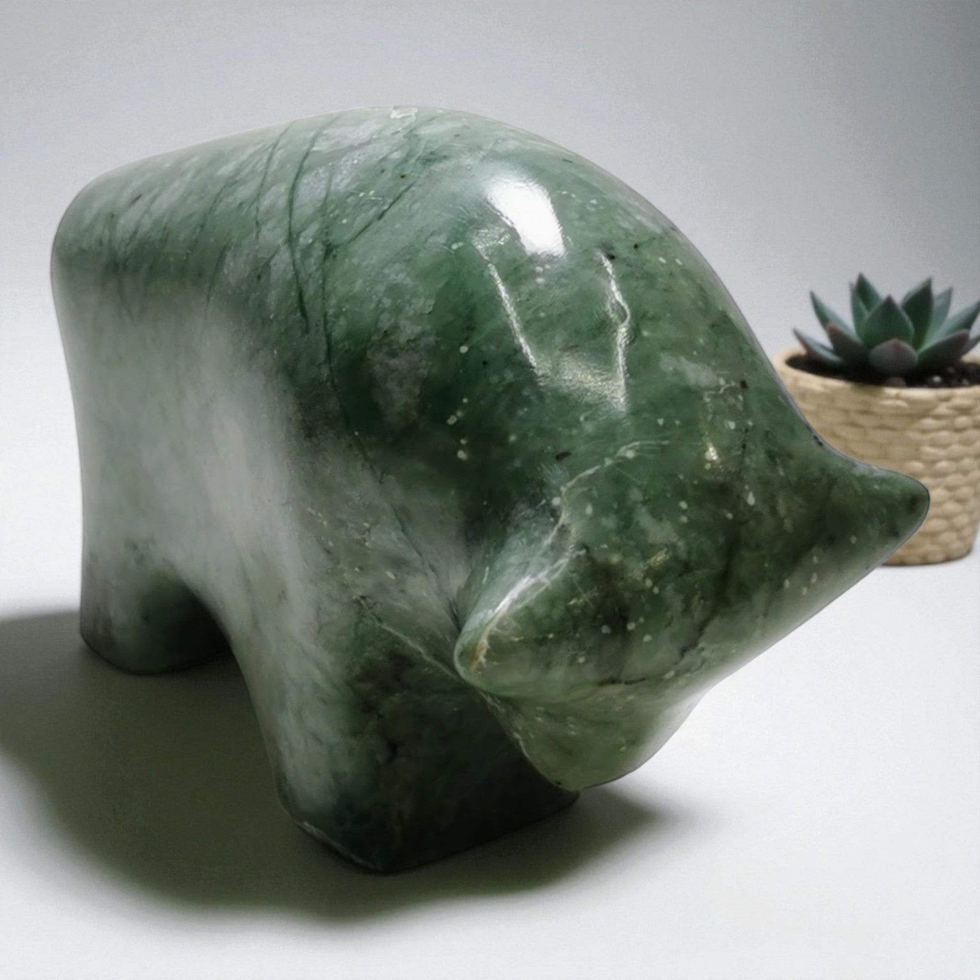 Green stone bear sculpture on a white surface with a plant in the background