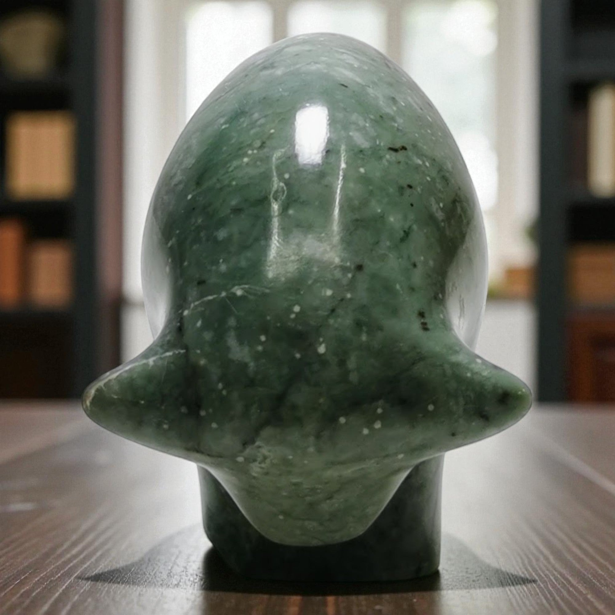 Green marble sculpture on a wooden surface with a blurred bookshelf background