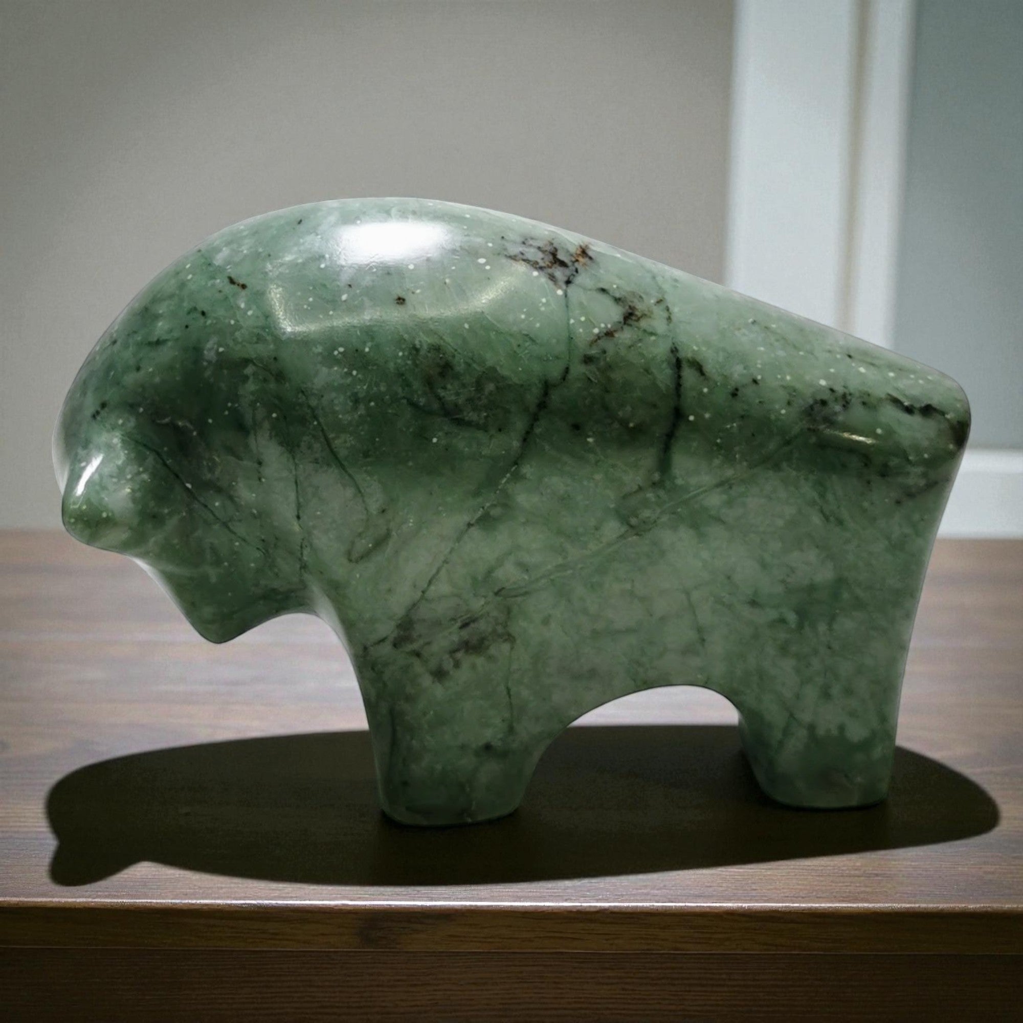 Green stone bear sculpture on a wooden surface with a neutral background