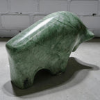 Green stone sculpture of a bear on a concrete floor with a white brick wall background