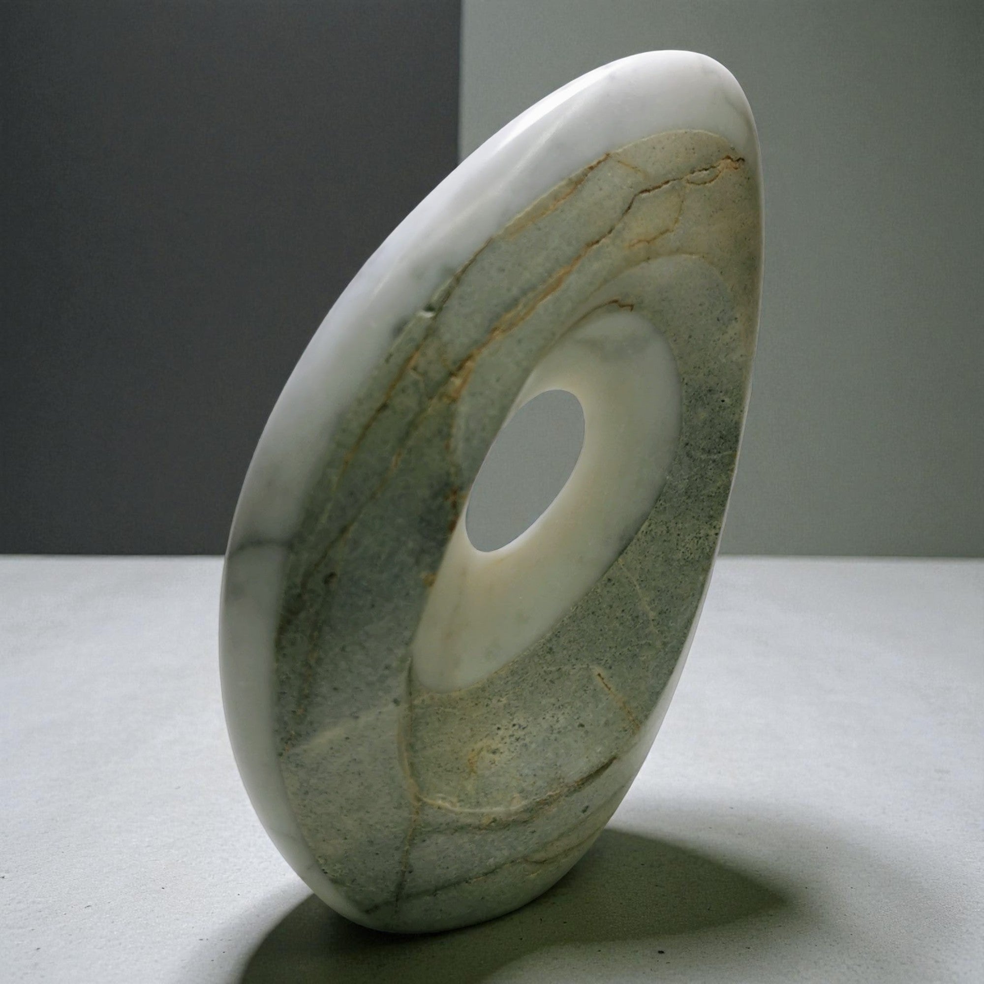 Abstract marble sculpture with smooth curved form and central void opening, polished
gray stone, contemporary luxury home decor art piece