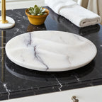 Marble-patterned soap dish on a black marble countertop with a plant and towel in the background.