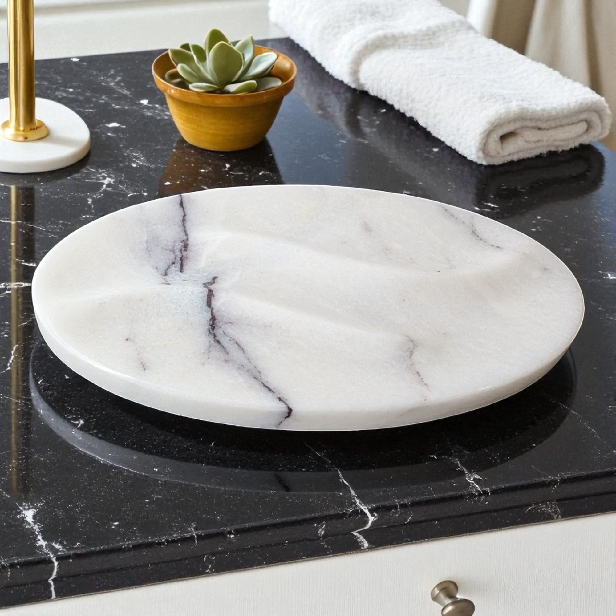 Marble-patterned soap dish on a black marble countertop with a plant and towel in the background.