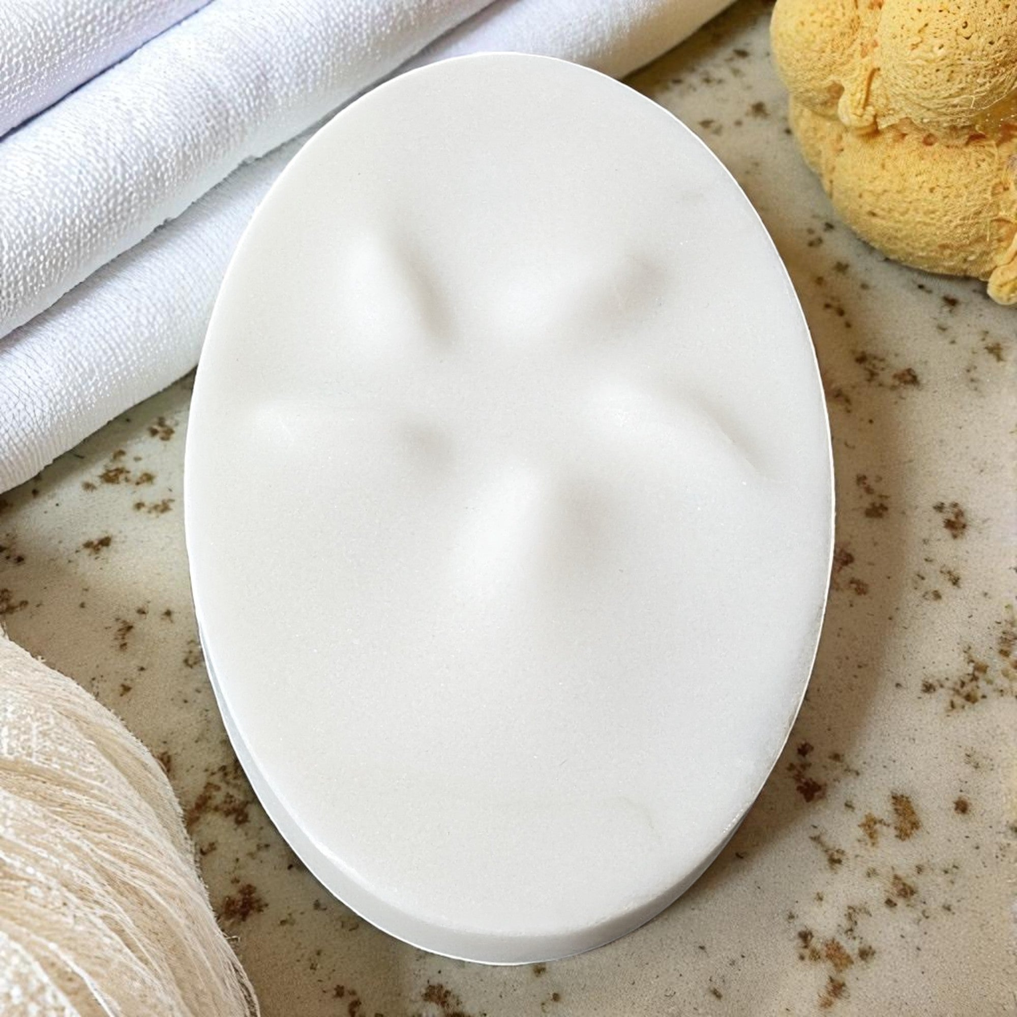 White soap bar on a textured surface with towels and a loofah in the background