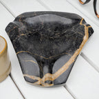 Geometric black and gold marble ashtray on a white wooden surface beside a candle