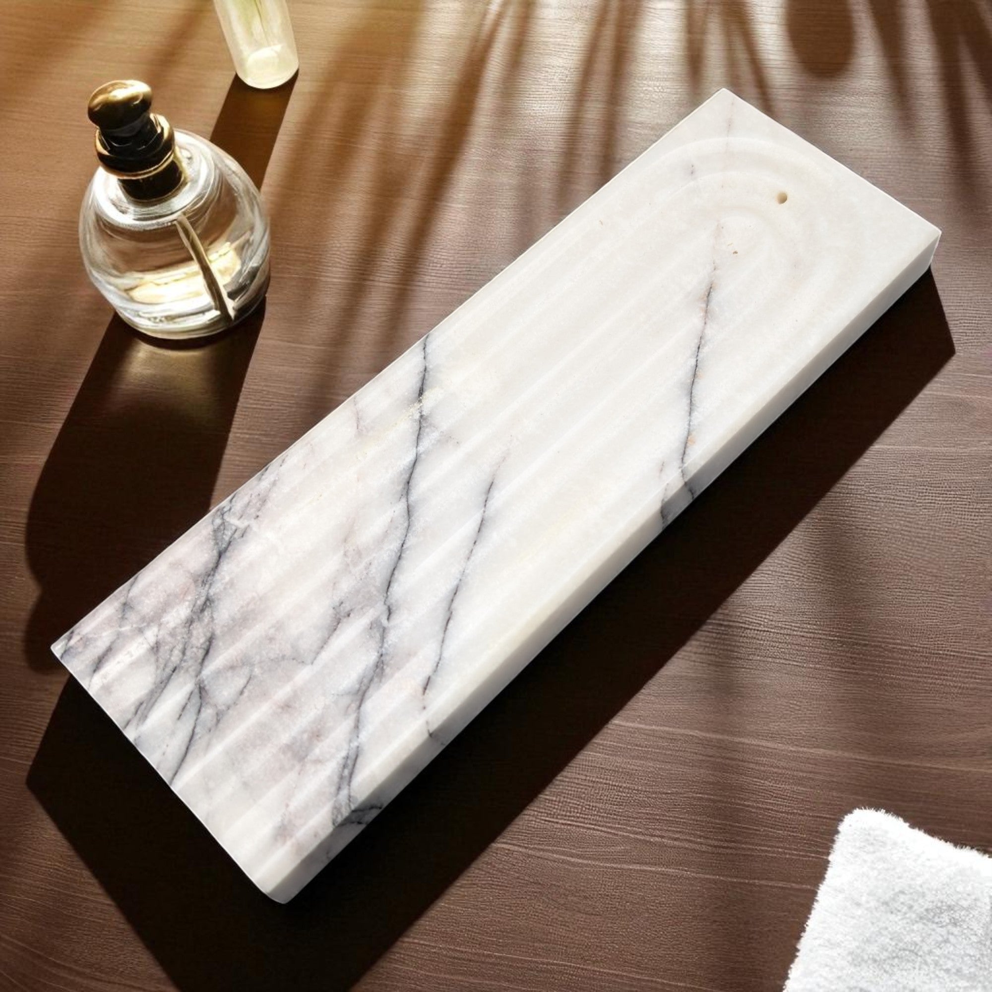 Marble tray on a wooden surface with a glass bottle and white towel.