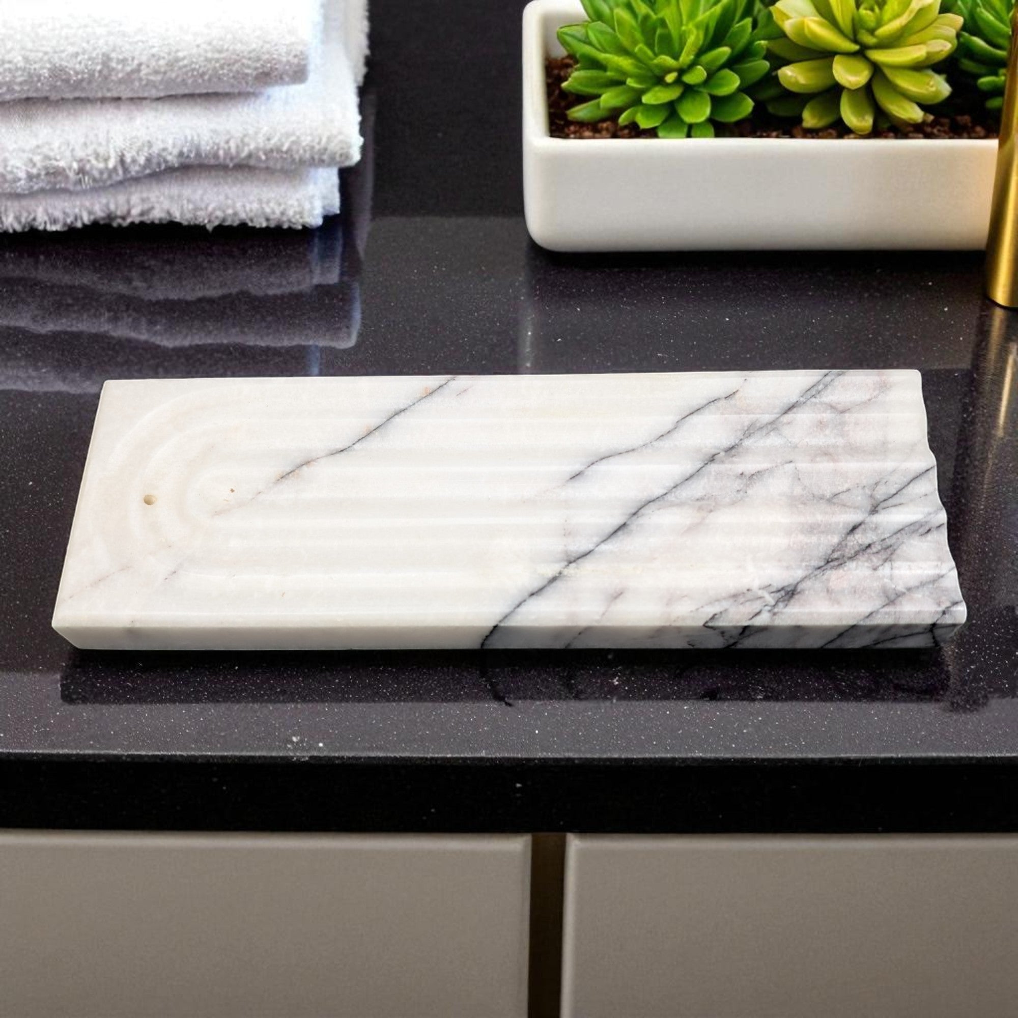 Marble-patterned incence stand on a black surface with towels and plants in the background