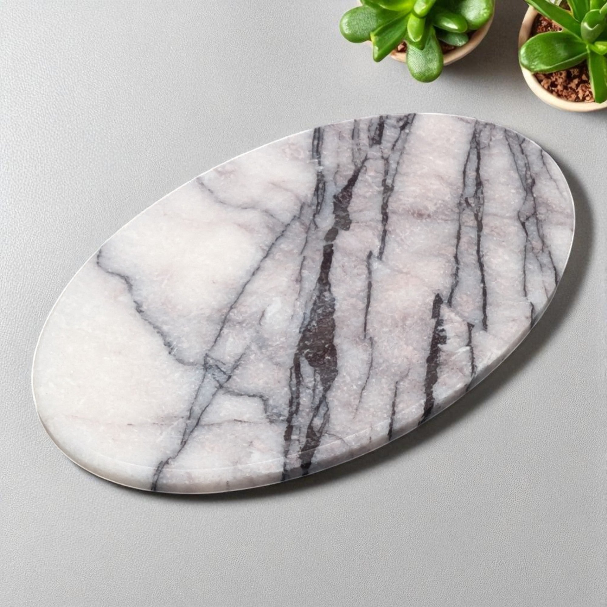 Marble-patterned soap dish on a gray surface with small potted plants.