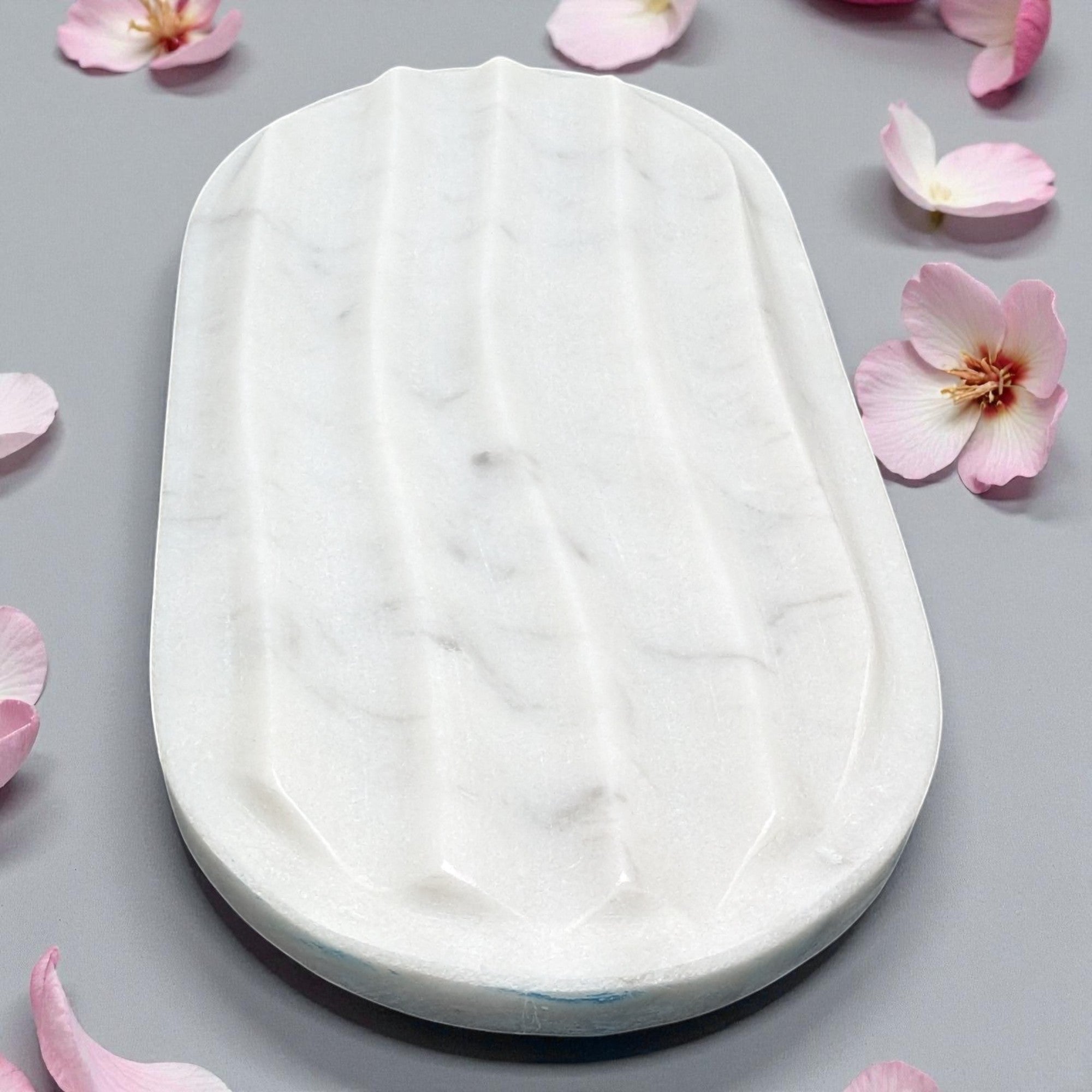 White soap bar on a gray surface with pink flower petals
