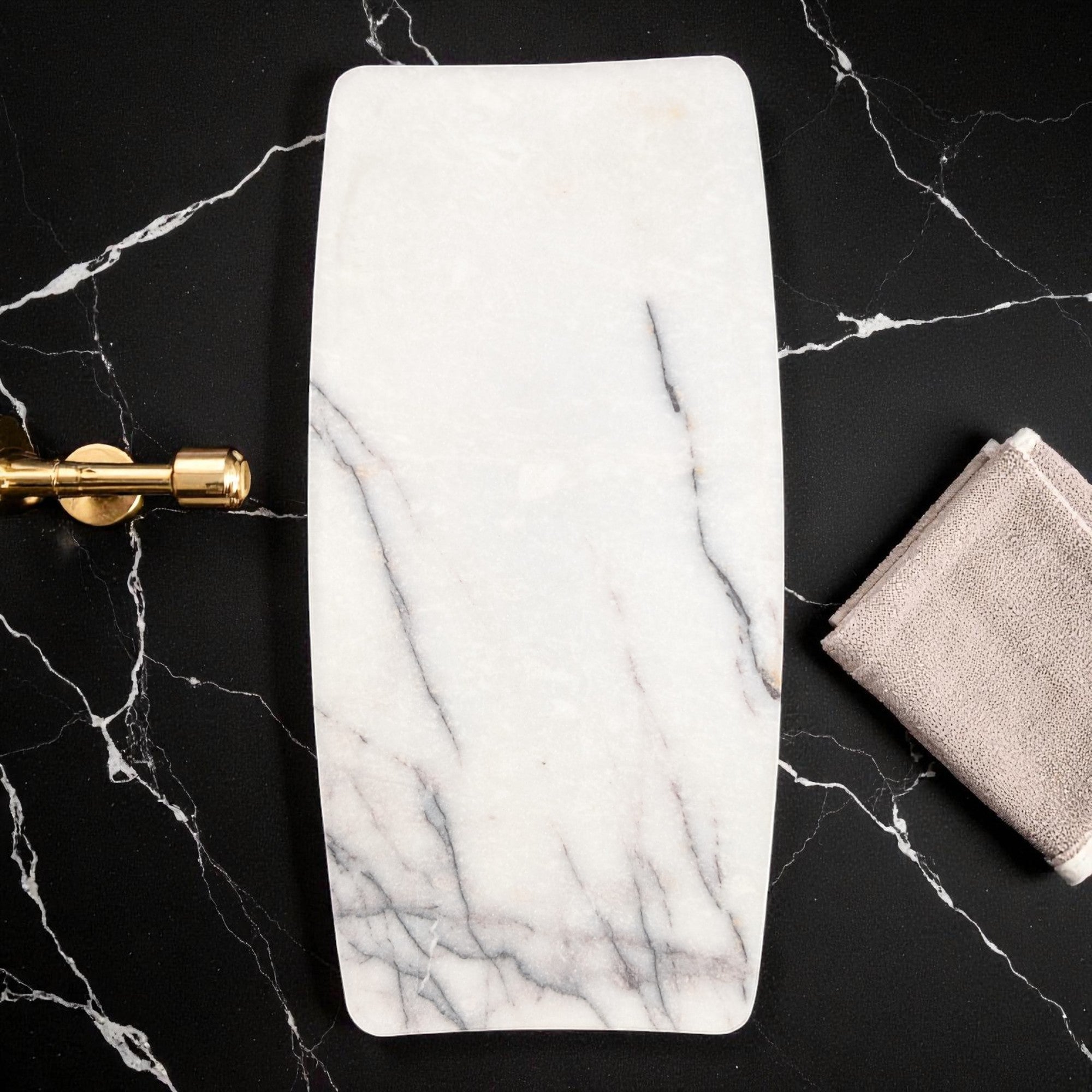 Marble vanity tray on a black marble surface with a towel and gold tool.