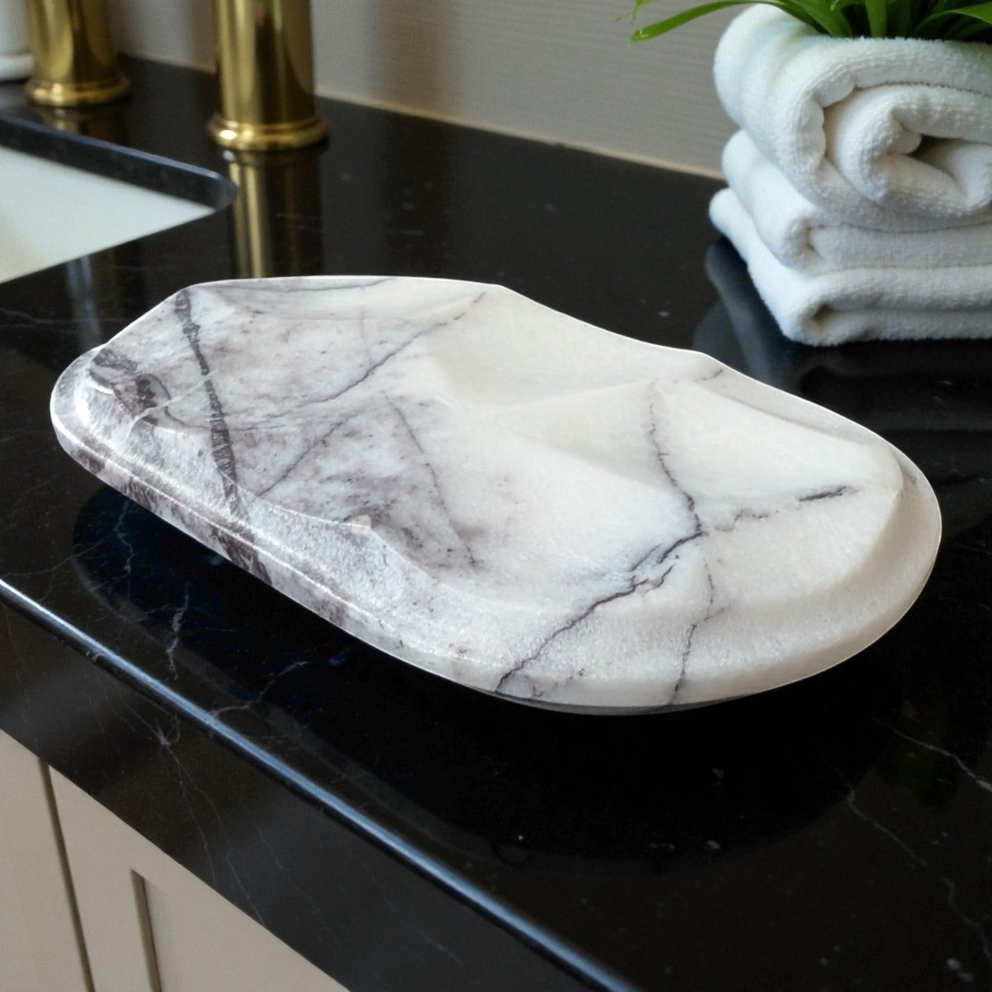 Marble-patterned soap dish on a black countertop with white towels in the background