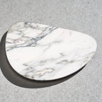 White marble jewelry tray, irregular shape, on a grey surface