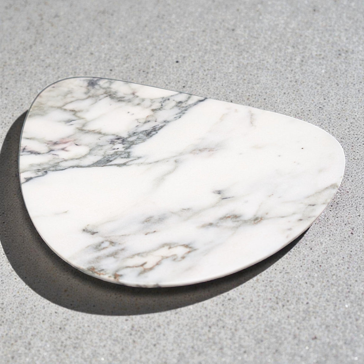 White marble jewelry tray, irregular shape, on a grey surface