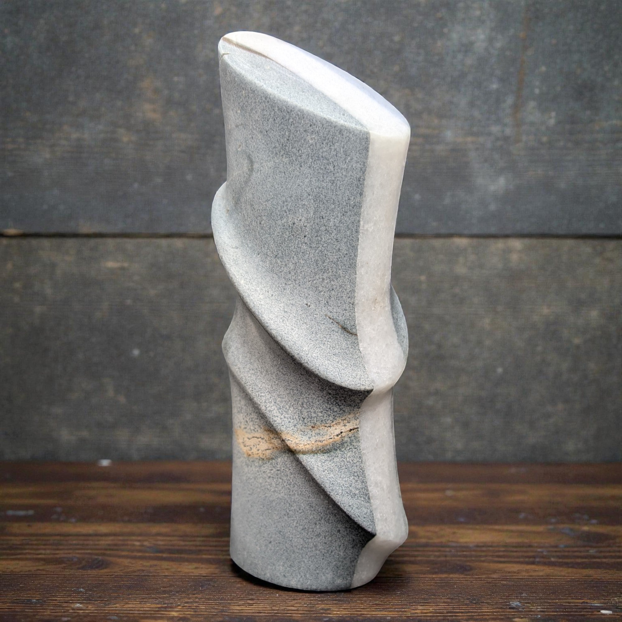 Gray stone sculpture on a wooden surface with a dark gray background