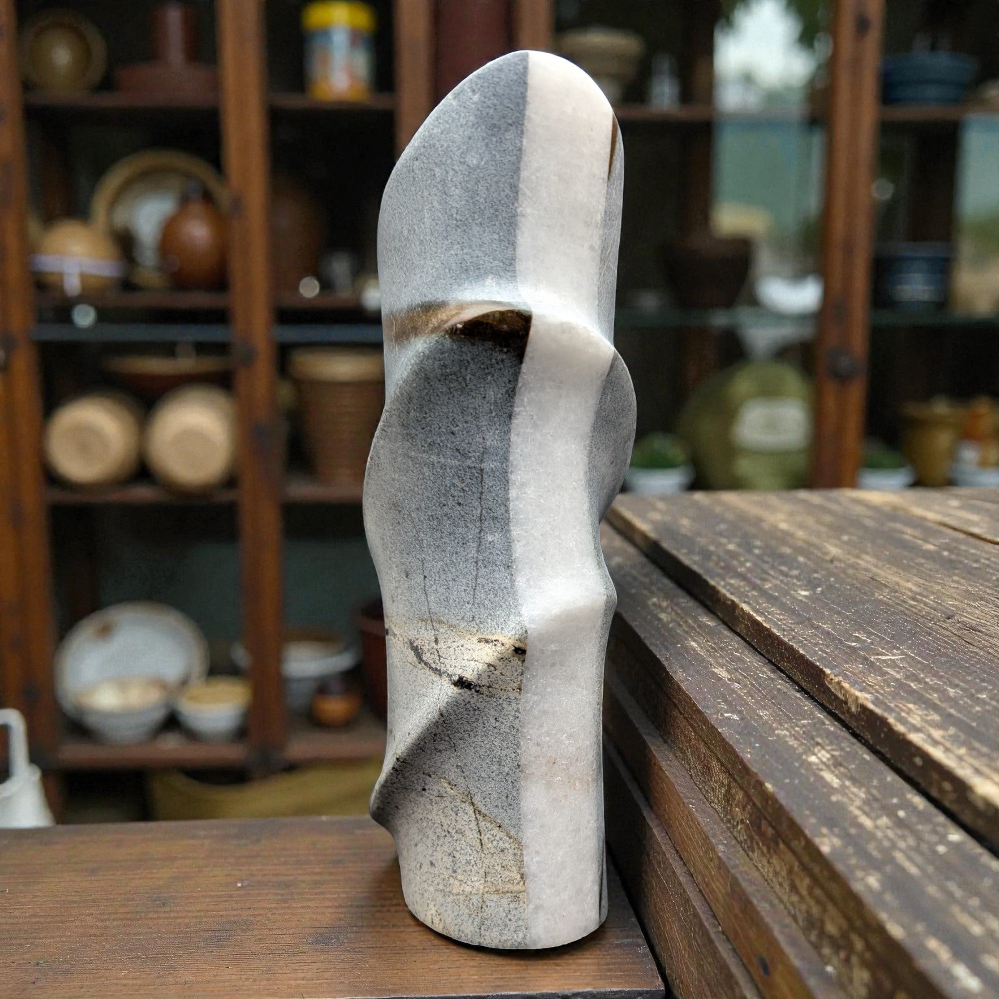 Ceramic shoe sculpture on a wooden table with shelves of pottery in the background