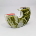 Green and white stone candle holder with two red candles on a light gray background