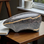 Decorative stone with gold inlay on a wooden surface next to an open book and a mug.