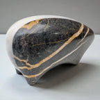 Decorative stone sculpture with black, gold, and white patterns on a gray background
