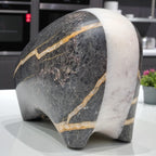 Marble sculpture of a bear on a reflective surface with a blurred indoor background